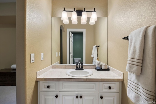 bathroom with a textured wall, vanity, and toilet