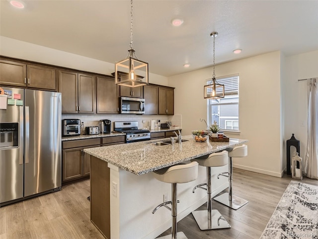 4955 Trails Edge Ln, Castle Rock, CO 80104 - kitchen with stainless steel appliances, light wood finished floors, dark brown cabinetry, a sink, and light stone countertops