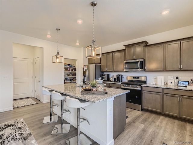 4955 Trails Edge Ln, Castle Rock, CO 80104 - kitchen with stainless steel appliances, light wood-type flooring, a kitchen island with sink, a breakfast bar area, and light stone countertops