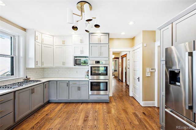 kitchen with gray cabinets, appliances with stainless steel finishes, hardwood / wood-style floors, and backsplash