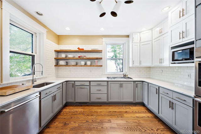 kitchen with sink, gray cabinets, hardwood / wood-style flooring, stainless steel appliances, and backsplash