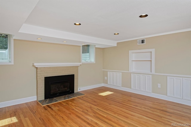 unfurnished living room featuring light wood-type flooring, ornamental molding, a brick fireplace, and a wealth of natural light