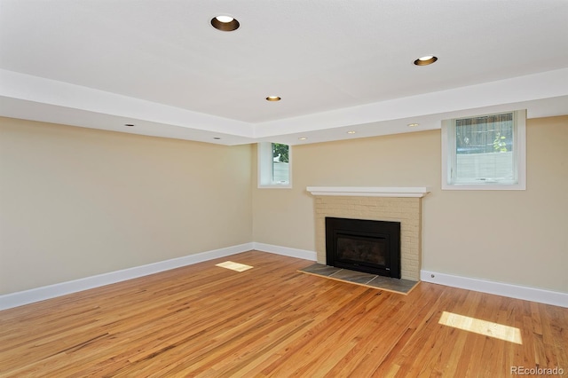 unfurnished living room featuring light wood-type flooring, a wealth of natural light, and a brick fireplace