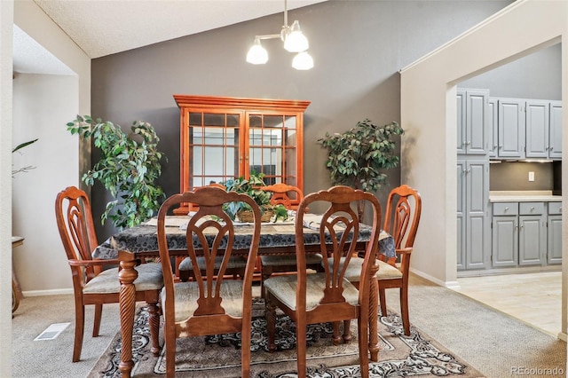 dining room with vaulted ceiling, light colored carpet, visible vents, and baseboards