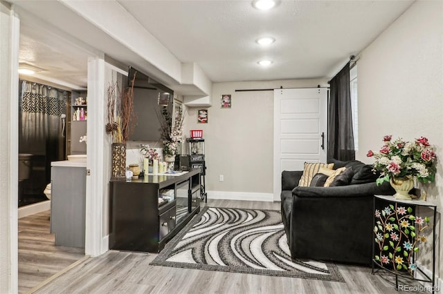 living room with a barn door, recessed lighting, wood finished floors, and baseboards