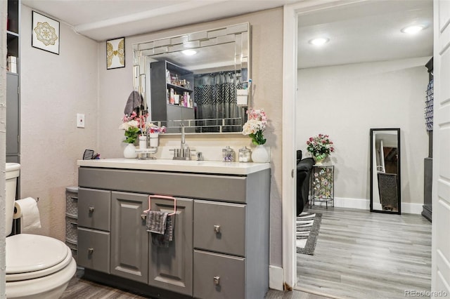 half bathroom with baseboards, toilet, wood finished floors, and vanity