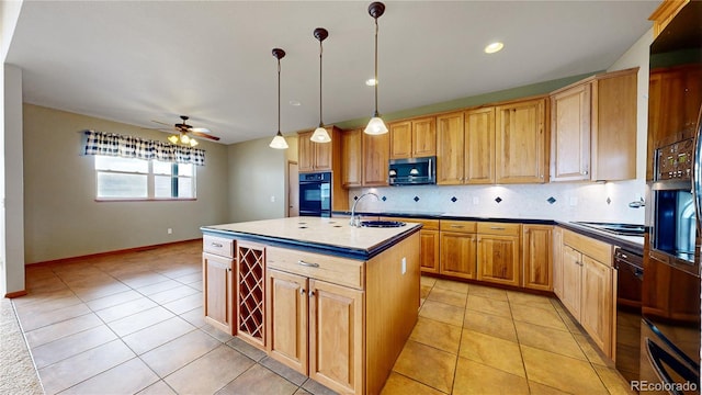 kitchen featuring sink, black oven, ceiling fan, decorative light fixtures, and an island with sink