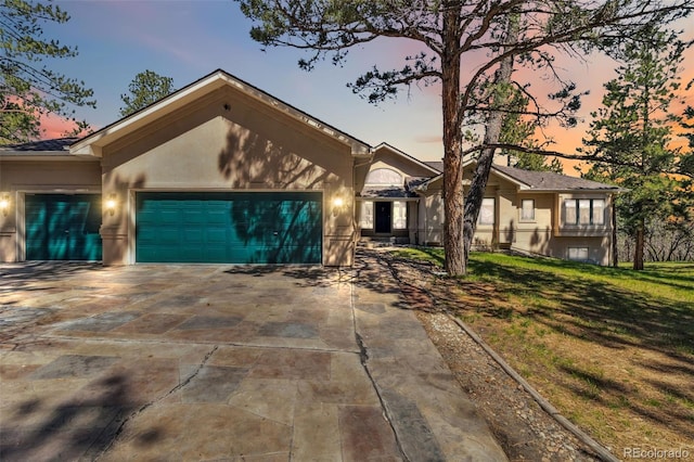 view of front of home featuring an attached garage, driveway, a yard, and stucco siding