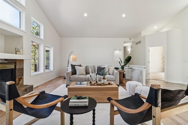 living room featuring high vaulted ceiling, a tile fireplace, recessed lighting, light wood finished floors, and baseboards