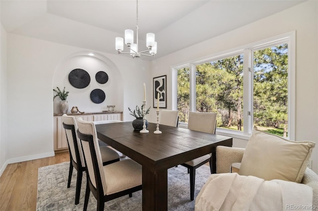 dining room featuring a chandelier, light wood-type flooring, baseboards, and arched walkways