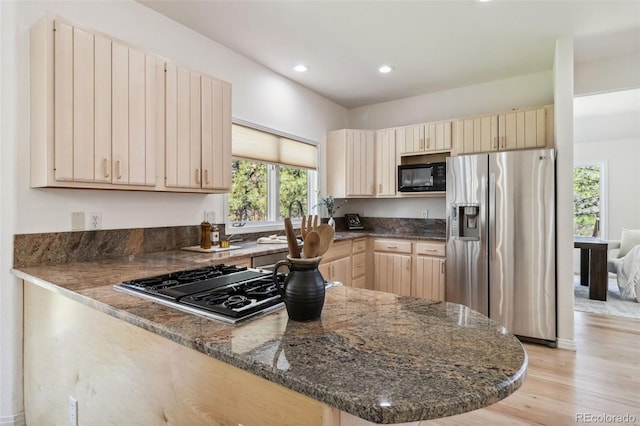 kitchen with stainless steel fridge with ice dispenser, stovetop with downdraft, black microwave, dark stone counters, and light wood finished floors