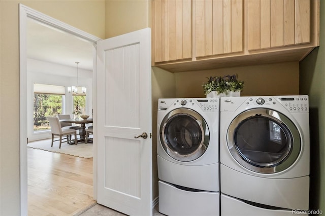 clothes washing area with washer and dryer, light wood-style flooring, cabinet space, and a chandelier