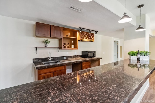 kitchen with a sink, black microwave, open shelves, pendant lighting, and track lighting