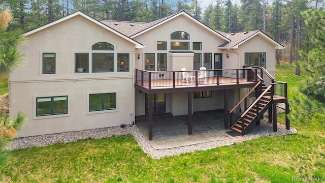 rear view of house featuring stucco siding, a patio, a wooden deck, and a lawn