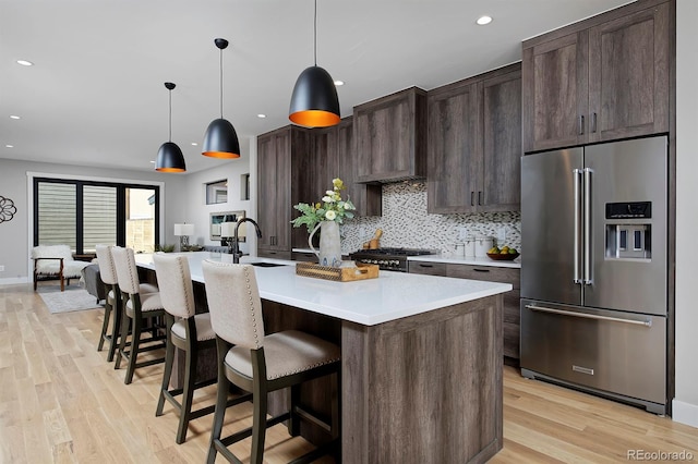 kitchen with an island with sink, dark brown cabinets, light hardwood / wood-style flooring, and stainless steel appliances