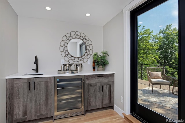 bar with dark brown cabinetry, light hardwood / wood-style floors, sink, and wine cooler