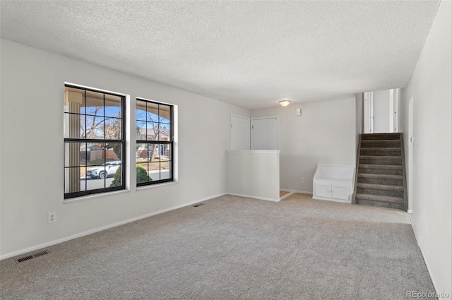 empty room with stairway, baseboards, visible vents, a textured ceiling, and light carpet