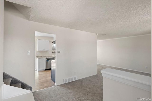 hallway with stairway, light colored carpet, visible vents, and a textured ceiling