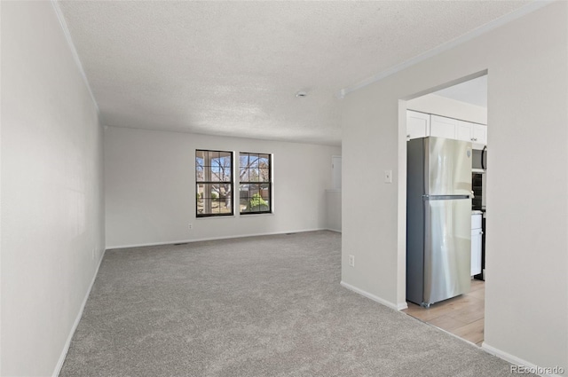 unfurnished room with light colored carpet, a textured ceiling, and baseboards