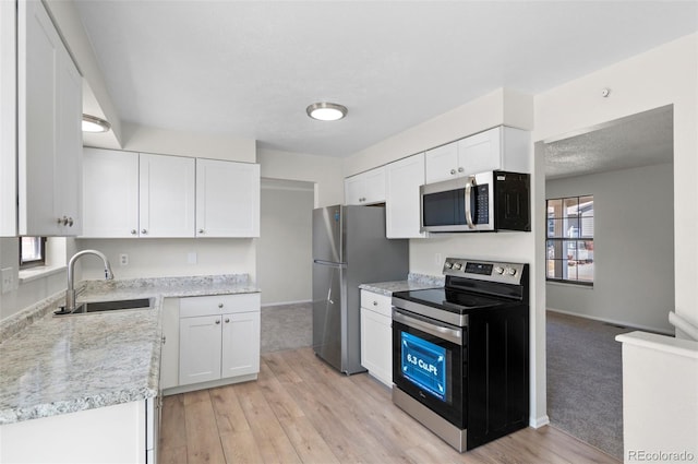 kitchen with baseboards, light wood-type flooring, appliances with stainless steel finishes, white cabinetry, and a sink