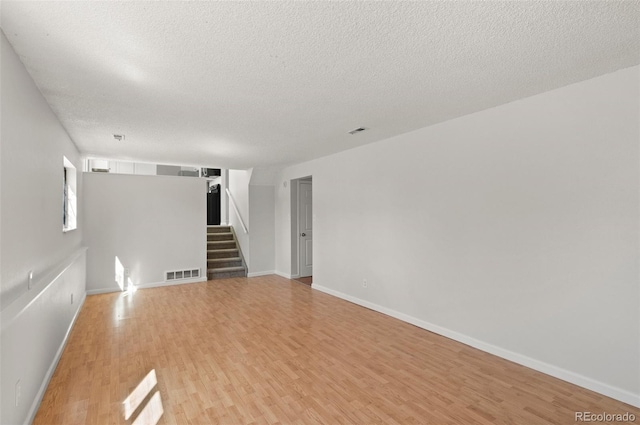 spare room with visible vents, a textured ceiling, light wood-style flooring, and stairway