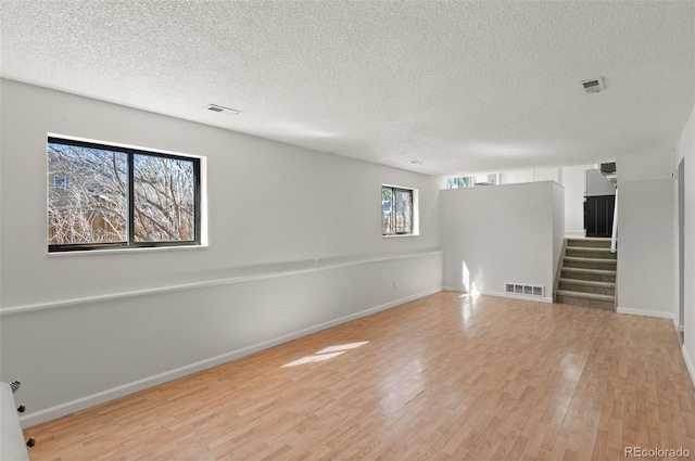 empty room featuring light wood finished floors, visible vents, stairway, and baseboards