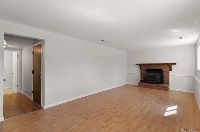 unfurnished living room featuring light wood-type flooring, baseboards, a textured ceiling, and a brick fireplace