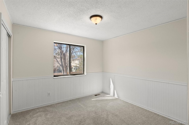 carpeted spare room featuring a wainscoted wall, a textured ceiling, and visible vents