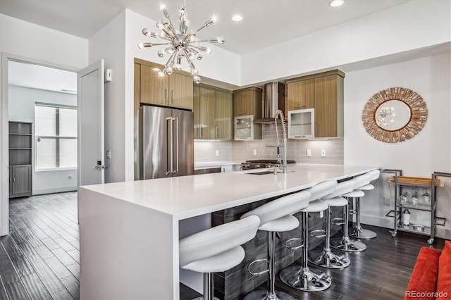 kitchen featuring wall chimney exhaust hood, a kitchen breakfast bar, dark hardwood / wood-style flooring, tasteful backsplash, and high quality fridge