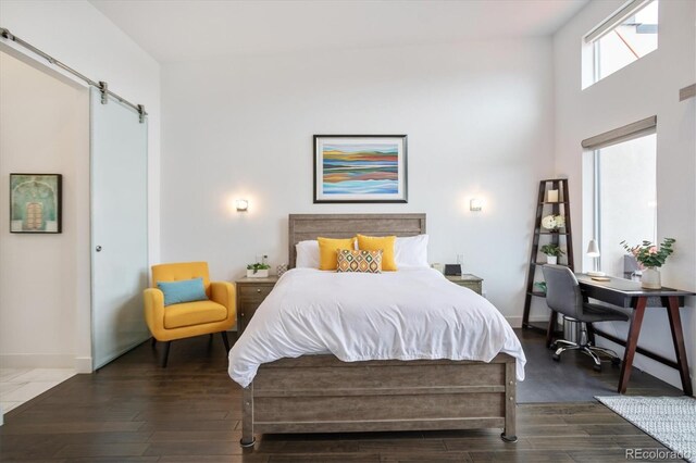 bedroom with a barn door, dark wood-type flooring, and a towering ceiling