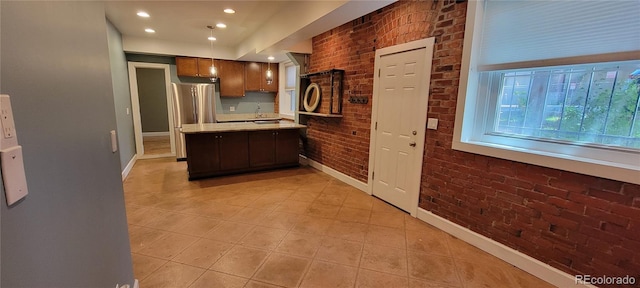 kitchen with light tile patterned flooring, brick wall, stainless steel refrigerator, sink, and dark brown cabinetry