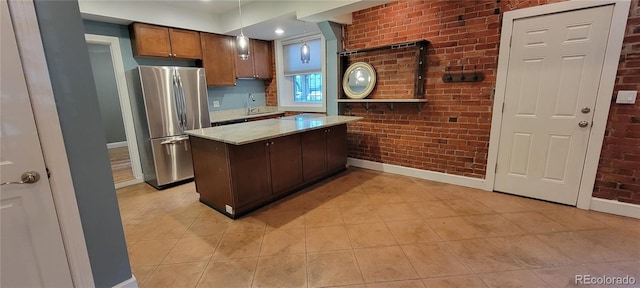 kitchen with hanging light fixtures, stainless steel fridge, light stone countertops, and brick wall