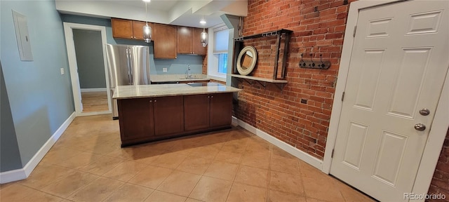 kitchen featuring sink, light tile patterned floors, stainless steel refrigerator, light stone counters, and brick wall