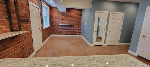 corridor featuring light tile patterned flooring and brick wall