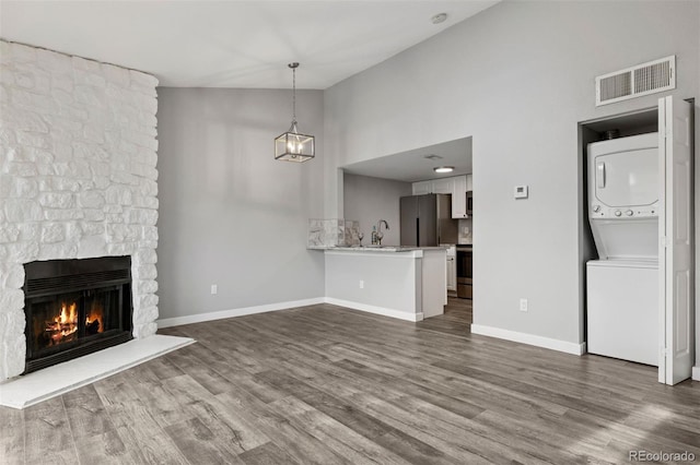 3100 S Federal Blvd Unit 331, Denver, CO 80236 - unfurnished living room with stacked washer / dryer, a stone fireplace, dark wood-style flooring, baseboards, and high vaulted ceiling