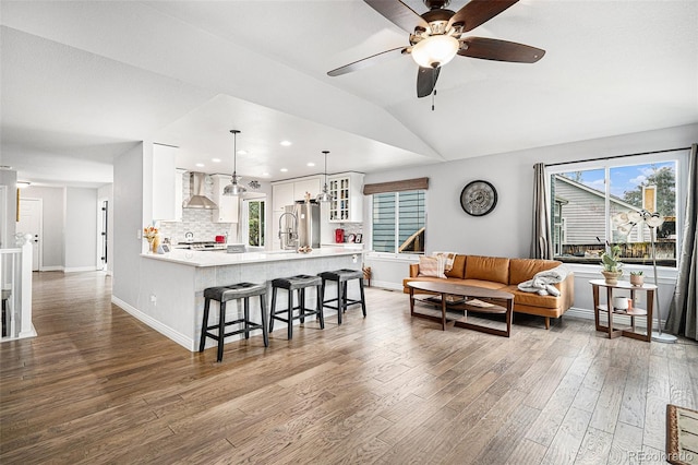 interior space with lofted ceiling, backsplash, wall chimney range hood, hanging light fixtures, and stainless steel fridge