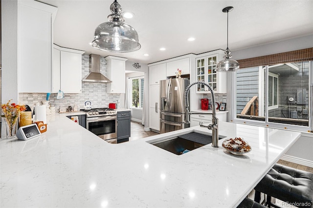 kitchen with white cabinetry, wall chimney exhaust hood, stainless steel appliances, decorative light fixtures, and a breakfast bar area