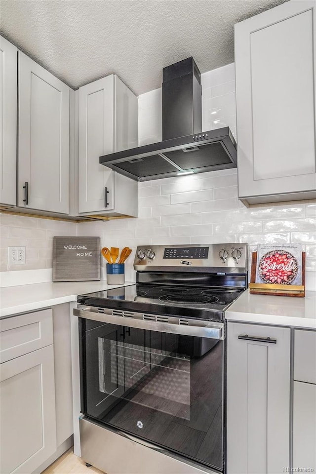 kitchen with white cabinetry, stainless steel range with electric stovetop, wall chimney exhaust hood, and a textured ceiling