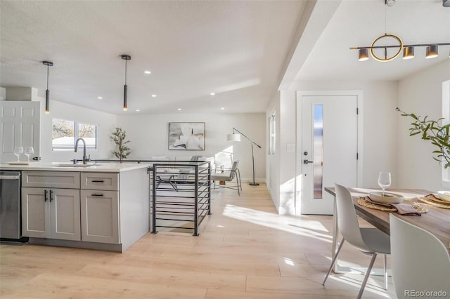 kitchen featuring gray cabinets, dishwasher, sink, hanging light fixtures, and light wood-type flooring