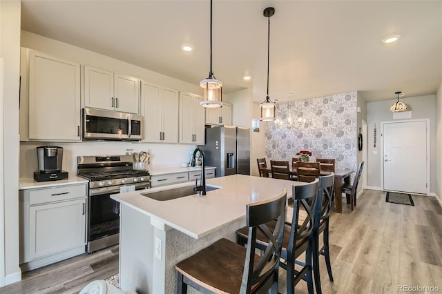 529 Beckwourth, Fort Lupton, CO 80621 - kitchen featuring appliances with stainless steel finishes, a center island with sink, light countertops, light wood-style flooring, and decorative light fixtures