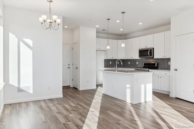 kitchen featuring appliances with stainless steel finishes, a center island with sink, white cabinetry, and hanging light fixtures