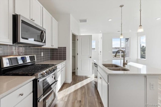 kitchen featuring appliances with stainless steel finishes, sink, a center island with sink, decorative light fixtures, and white cabinetry