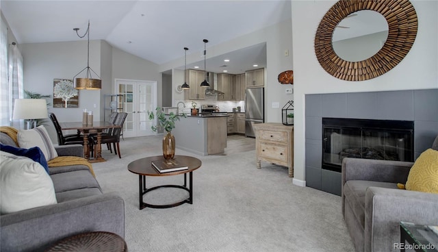 carpeted living room featuring french doors, high vaulted ceiling, a tiled fireplace, and sink