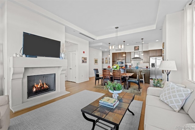 living room with light wood-type flooring and a raised ceiling