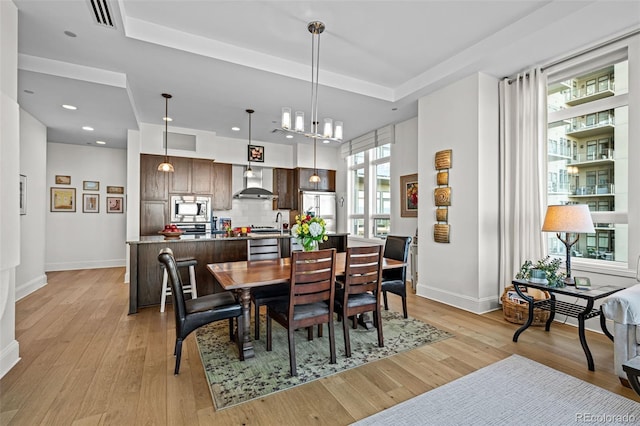 dining area featuring a tray ceiling, light hardwood / wood-style flooring, and an inviting chandelier