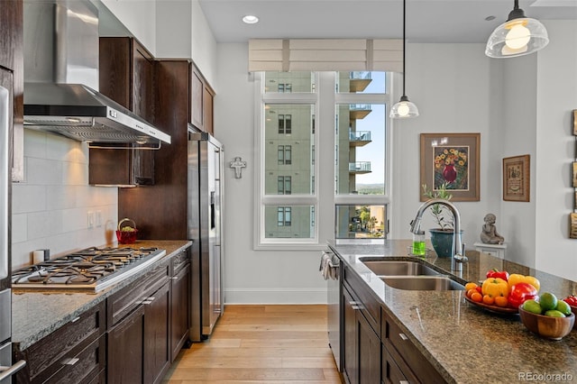 kitchen with dark stone countertops, wall chimney range hood, stainless steel appliances, and hanging light fixtures