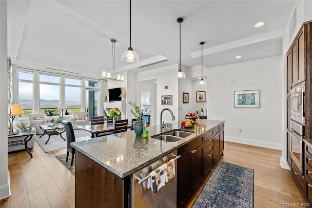 kitchen with sink, stainless steel appliances, a center island with sink, and light wood-type flooring