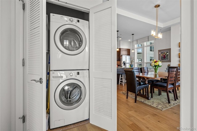 clothes washing area featuring a chandelier, stacked washer and clothes dryer, and light wood-type flooring