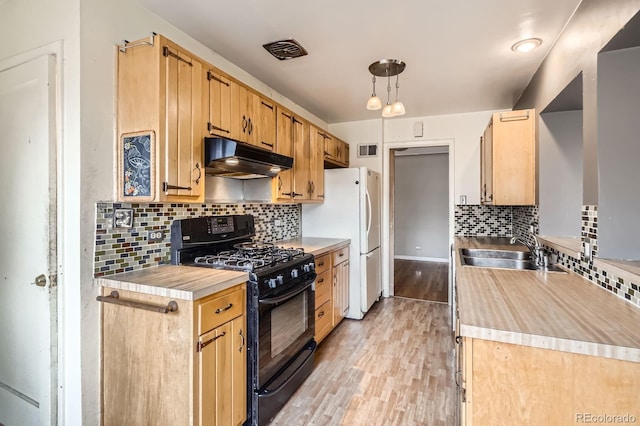 kitchen with a sink, decorative backsplash, under cabinet range hood, visible vents, and black gas range