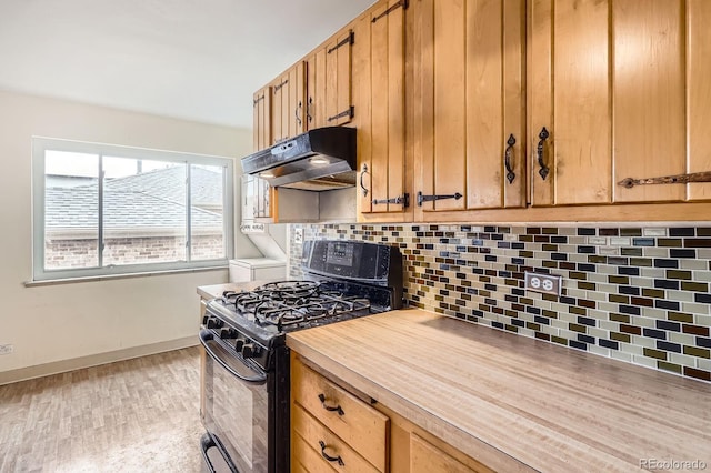 kitchen with backsplash, light countertops, baseboards, black range with gas stovetop, and under cabinet range hood